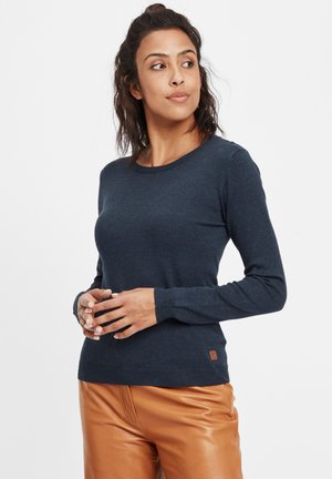 Pull marin à manches longues avec un col rond, fabriqué en tissu tricoté lisse; présente une petite écusson logo près de l'ourlet et des poignets côtelés.