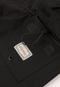 Schwarzer Stoff mit glatter Textur, versehen mit einem Reißverschluss, Klettverschluss-Patches und einem Etikett mit der Aufschrift "Rivvia", umgeben von einem grünen Blumenmotiv.