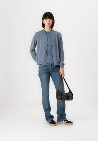 Lys blå bomberjakke, lange ermer, glidelås; kombinert med en lys blå topp og blå jeans. Svart og hvit sneakers, liten brun håndveske.