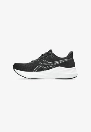 Chaussure de sport noire avec une tige en maille texturée, semelle intermédiaire blanche et semelle extérieure noire. Elle présente un logo argenté et des accents de couture contrastants.