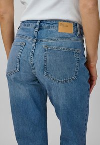 Ljusblå jeans med hög midja, klassisk femfickdesign och en läderlapp på baksidan av midjan. Slät denimtextur.
