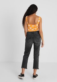 Top de tirantes naranja con estampado floral combinado con jeans negros de cintura alta con dobladillo sin terminar. Zapatillas negras completan el conjunto.