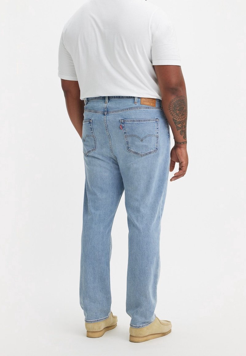 Jeans de mezclilla azul claro con diseño de pierna recta, que cuentan con un parche de cuero en la parte posterior, cuatro bolsillos y detalles de costura visibles.