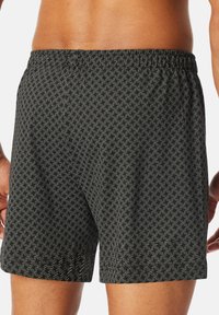 Shorts de bain noirs à motif avec un design géométrique, dotés d'une taille élastique et d'une coupe décontractée, fabriqués en tissu léger.