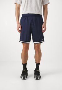 Pantalones cortos de baloncesto Nike en color navy con cinturilla elástica, franjas laterales blancas y textura suave. Combinados con zapatillas negras y calcetines estampados.