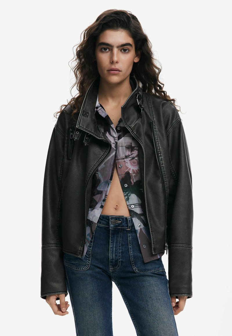 Black leather motorcycle jacket with an asymmetrical zip, structured shoulders, and prominent stitching details, worn over a patterned shirt.