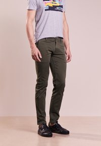 Olivgröna slim-fit byxor i bomull, med framfickor och en enkel design, matchade med svarta sneakers.