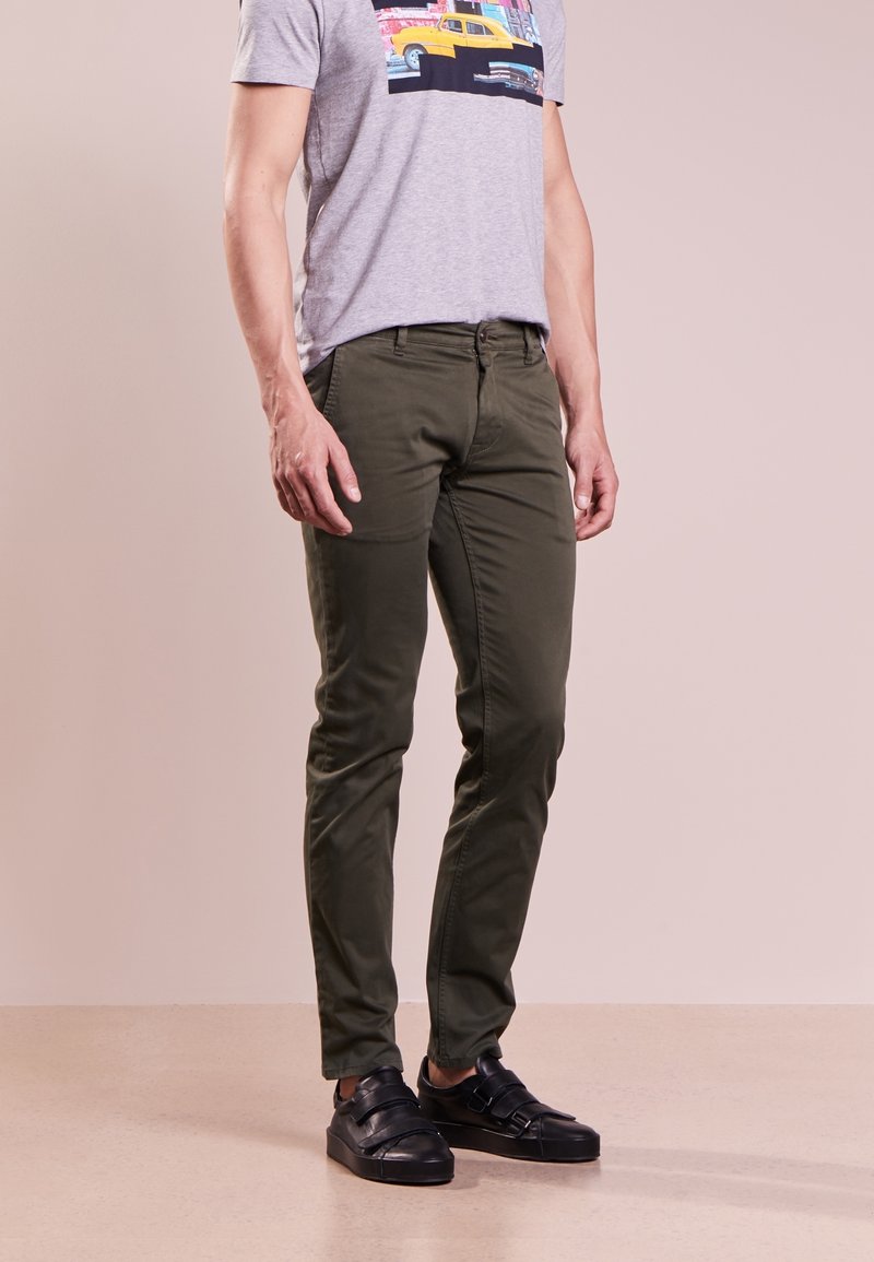 Olivgröna slim-fit byxor i bomull, med framfickor och en enkel design, matchade med svarta sneakers.