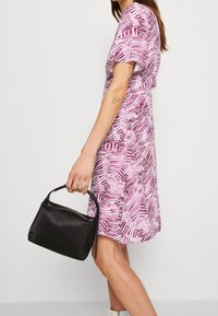 Kortärmad klänning i rosa med ett geometriskt mönster, kombinerad med en liten svart handväska och ankelboots; slätt tyg och figursydd form.