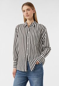 Schwarz-weiße gestreifte Hemdbluse mit langen Ärmeln, einer Brusttasche und einem lässigen Schnitt, kombiniert mit blauen Jeans.