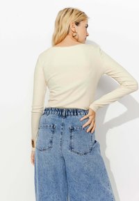 Chemise beige clair à manches longues associée à un pantalon large en denim bleu clair taille haute, doté d'une taille élastique et de poches arrière.