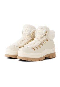 Białe buty turystyczne z kołnierzem z imitacji futra, złotymi elementami i sznurowaniem. Gruba beżowa podeszwa z teksturowanym bieżnikiem zapewniającym przyczepność.