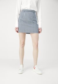 Karierte Minirock aus blau-weißem Stoff, taillierte Passform mit hoher Taille. Getragen mit weißen Sneakern mit roten Akzenten.