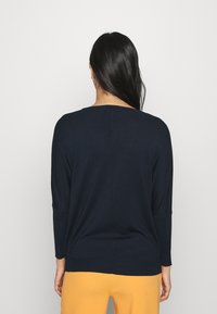 Pull en tricot bleu marine, à coupe décontractée, col rond et manches trois-quarts. Texture lisse avec un détail de couture centrale.