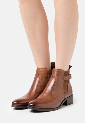 Brązowe skórzane botki na kostkę z bocznymi elastycznymi panelami i ozdobnym paskiem, wyposażone w niski obcas typu słupek oraz gładkie wykończenie.