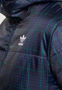 Navy puffer jacket with green plaid pattern, featuring a high collar and zip closure; includes white Adidas logo on the chest.