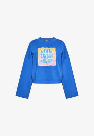 Sininen huppari pitkillä hihoilla, jossa on keskellä graafinen kuvasto, johon kuuluu teksti "ELÄ UNELMASI" värikkäällä, rohkealla fontilla.