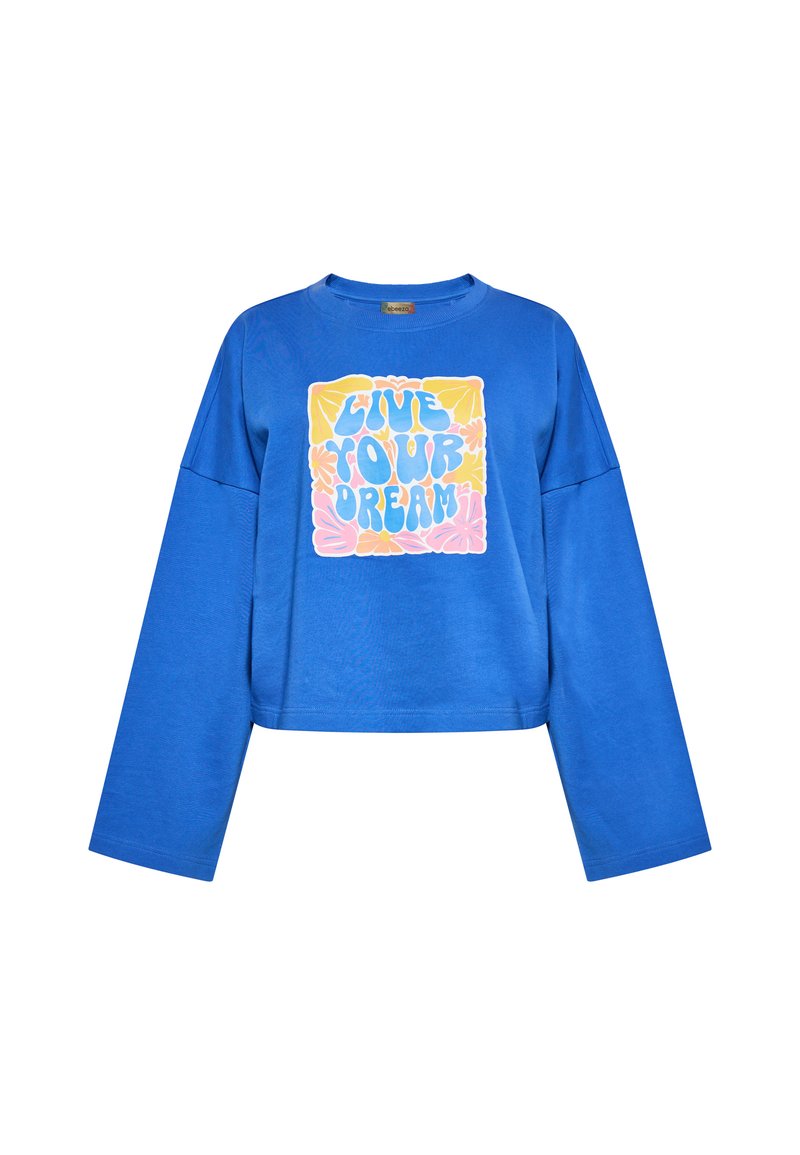 Sininen huppari pitkillä hihoilla, jossa on keskellä graafinen kuvasto, johon kuuluu teksti "ELÄ UNELMASI" värikkäällä, rohkealla fontilla.