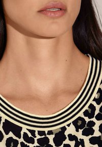 Leopardprint gebreid top met een ronde halslijn en een zwart-wit gestreepte ribbelkraag. Gladde textuur, natuurlijke huidtinten zichtbaar.