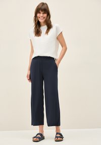 Witte gestructureerde top met korte mouwen, gecombineerd met marineblauwe wijde cropped broek, met zijzakken en een relaxte pasvorm. Gemaakt met donkere sandalen.