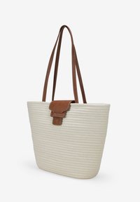 Bolso tote confeccionado en tela natural tejida, con un cierre de solapa de cuero marrón y dos asas para llevar al hombro. Color crema con un diseño texturizado.