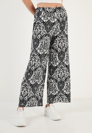 Schwarz-weiße gemusterte weit geschnittene Hose mit einem Blumen- und Blätterdesign. Hergestellt aus leichtem Material mit einem elastischen Bund.