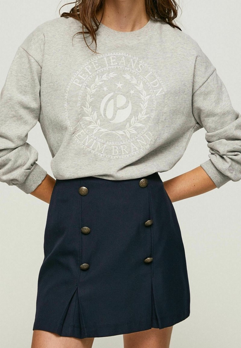 Sweat-shirt gris Pepe Jeans avec logo blanc et mini-jupe taille haute bleu marine avec deux rangées de boutons métalliques décoratifs.