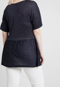 Marinblus med korta ärmar, med ett texturerat stickmönster och samlat midja. Kombinerad med vita byxor för kontrast.