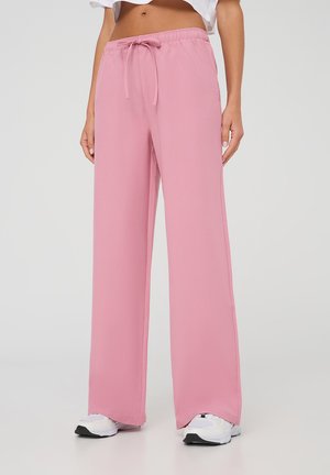 Pantaloni palazzo rosa in tessuto morbido con cintura elastica e cordoncino. Abbinati a sneaker bianche.