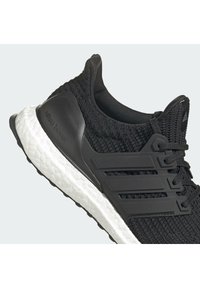Chaussure de course noire tricotée avec semelle blanche texturée, soutien de talon en plastique noir et lacets noirs, vue de côté.