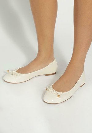 Cream patent ballet flats with a rounded toe, decorative bow detail, and small gold accent. Flat sole and smooth, glossy texture.