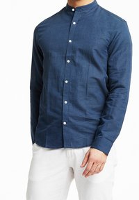 Marineblauwe blouse met lange mouwen, een bandkraag, knoopsluiting en een textuur stof. Draag het met lichtgekleurde broeken, wat een getailleerde silhoutte toont.
