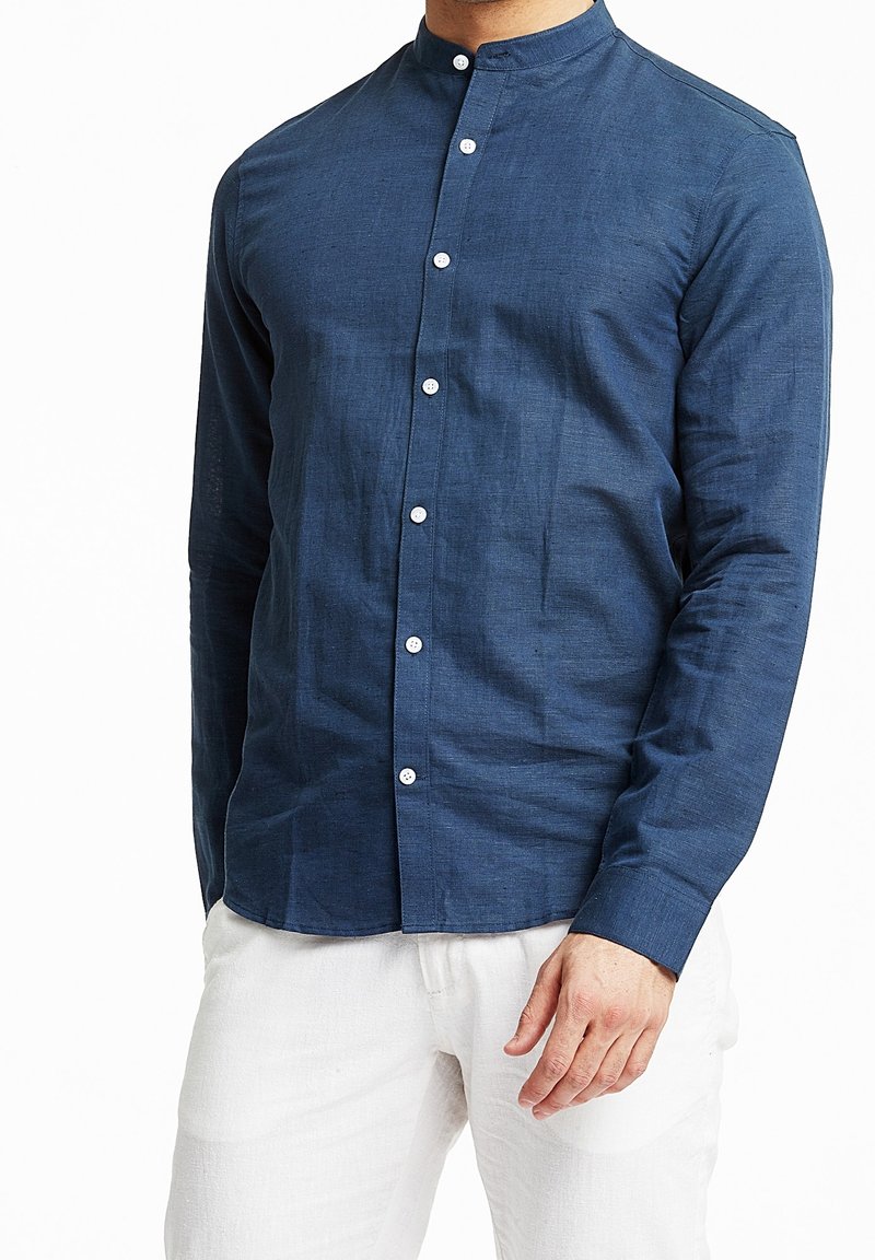 Marineblauwe blouse met lange mouwen, een bandkraag, knoopsluiting en een textuur stof. Draag het met lichtgekleurde broeken, wat een getailleerde silhoutte toont.