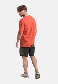T-shirt en coton orange à manches courtes, associé à un short noir avec des poches cargo vertes. Porté avec des baskets grises.