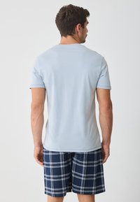 Light blue cotton t-shirt with short sleeves, paired with navy plaid shorts featuring white lines. Casual fit, plain design, no graphics.