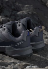 Ζευγάρι γκρίζα παπούτσια Adidas Terrex για ορεινό τρέξιμο τοποθετημένα σε βραχώδες έδαφος έξω.