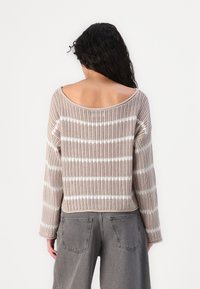 Stickad tröja i beige med vita horisontella ränder, med en bred halsringning, långa ärmar och en avslappnad passform. Texturerad väv ger dimension.