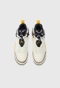 Zapatillas altas en blanco y negro con acentos amarillos y morados, cuero texturizado, diseño de cordones y patrón de suela visible.
