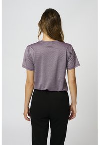 Lila kortärmad t-shirt med en subtil lyster, rund hals och avslappnad passform, tillsammans med svarta byxor. Slät textur utan synliga mönster.