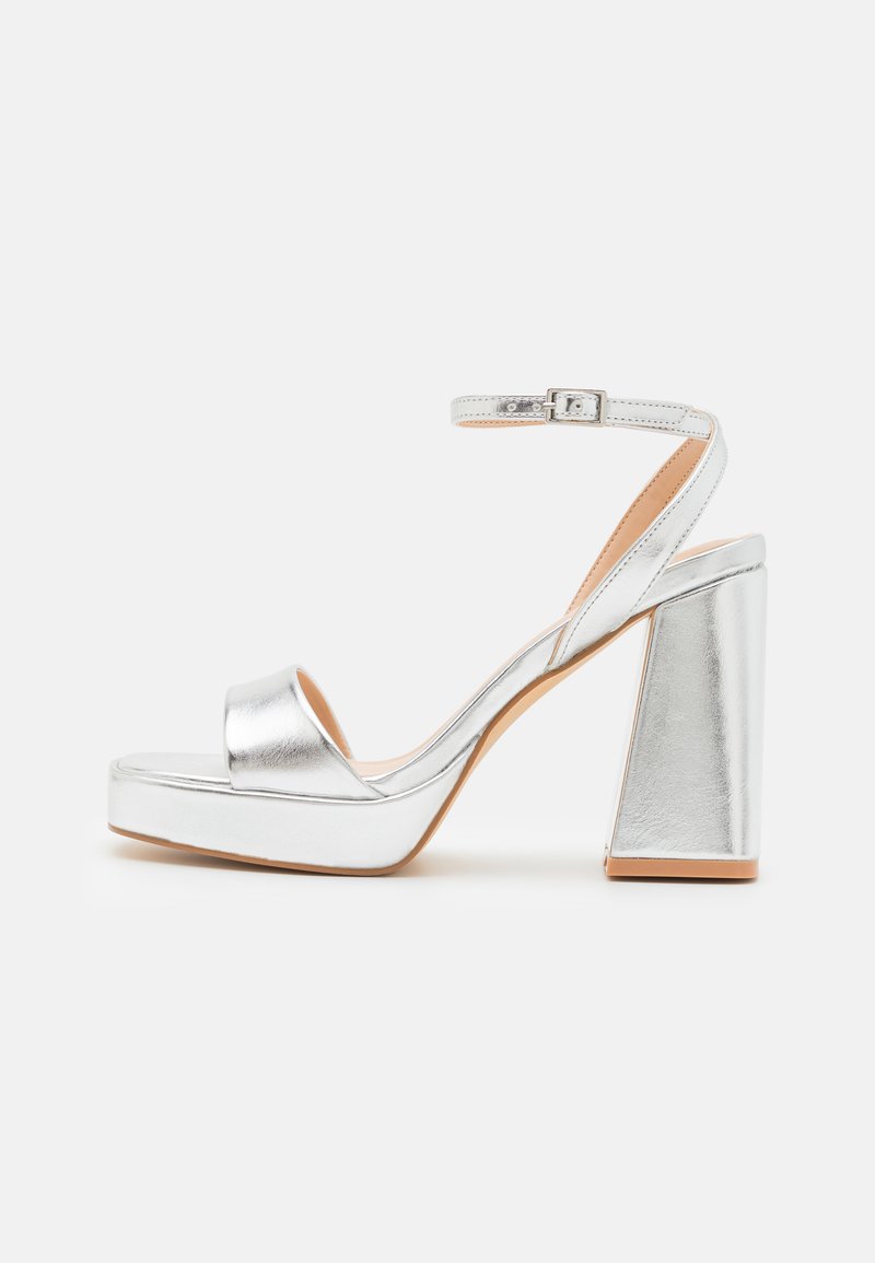 Silver platform sandals with a wide toe strap, ankle strap with buckle, and a chunky heel. Smooth metallic finish and flat sole design.