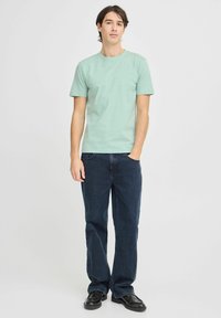 Lys grønn bomulls t-skjorte kombinert med mørkeblå denim jeans. Antrekket har en klassisk rund halslinning og en avslappet passform. Sorte sko fullfører stilen.