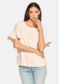 Helles rosa Blusenshirt mit ausgestellten kurzen Ärmeln, rundem Ausschnitt und glatter Textur. Kombiniert mit hellblauen Jeans für einen lässigen Look.