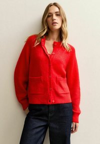 Röd stickad cardigan med långa ärmar, rund hals och knappstängning, med två framfickor och en mjuk, texturerad yta.