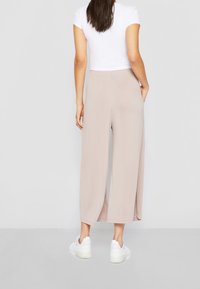 Pantalons larges beiges avec une taille élastique, des poches latérales et une texture lisse. Portés avec un t-shirt blanc court et des baskets blanches.