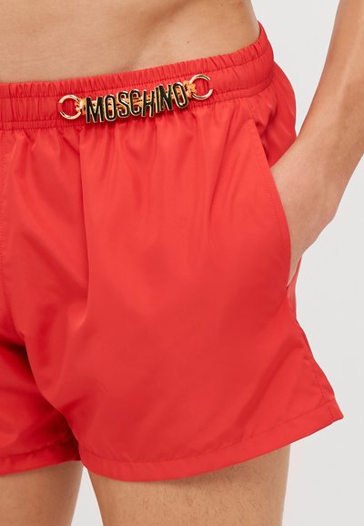 Shorts de bain rouges en tissu lisse, dotés d'une taille élastique avec un logo Moschino doré à l'avant et de poches latérales.