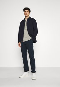 Marineblå skjorte med knapper over en grå t-skjorte, kombinert med mørke bukser og hvite joggesko. Rene linjer og avslappet passform.