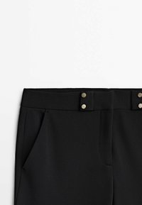 Pantalon noir sur mesure avec poches latérales et une ceinture ornée de deux boutons-pression argentés sur un fond blanc.