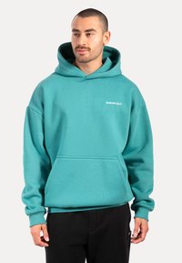 Felpa turchese con tasca a marsupio, polsini e orlo a coste; presenta un logo bianco sul petto e un cappuccio con cordino.