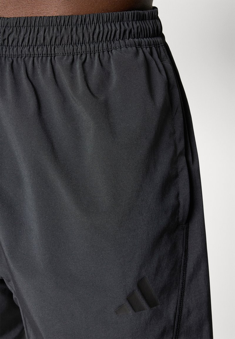 Zwarte sportbroek met een elastische tailleband, voorzien van een gladde textuur en een tonale Adidas-logo aan de zijkant. Geen opvallende patronen.