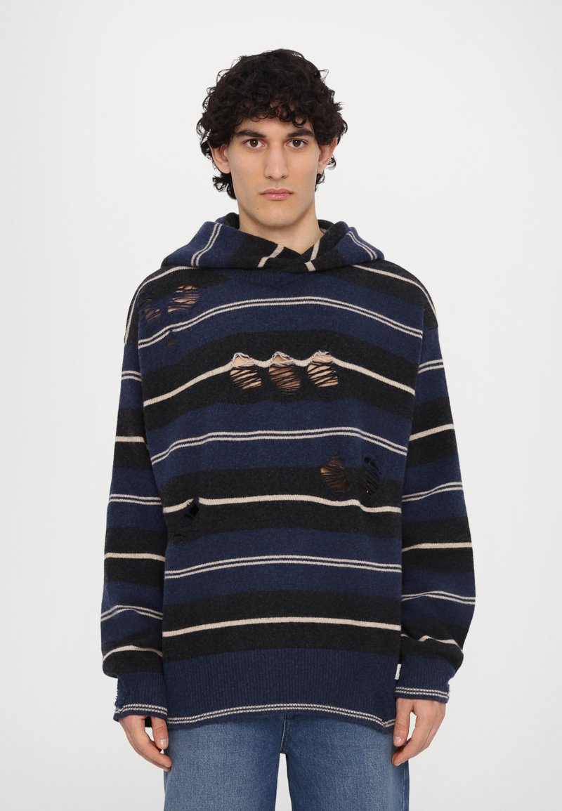 Sweat à capuche en tissu tricoté avec des rayures bleu foncé, marine et crème, comportant des patchs usés et une coupe décontractée.